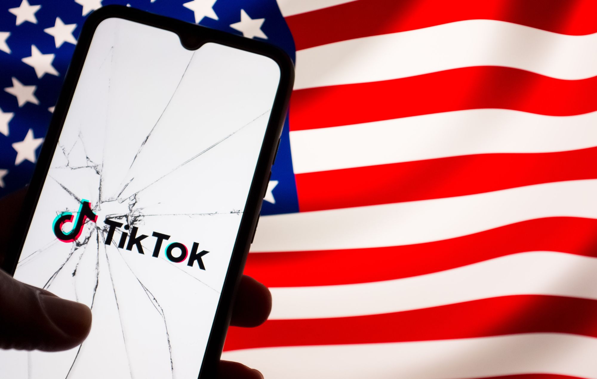 Sur cette photo d'illustration, le logo TikTok est affiché sur l'écran d'un téléphone vu à travers du verre brisé, avec un drapeau américain apparaissant sur un écran en arrière-plan à Athènes, en Grèce, le 25 avril 2024.