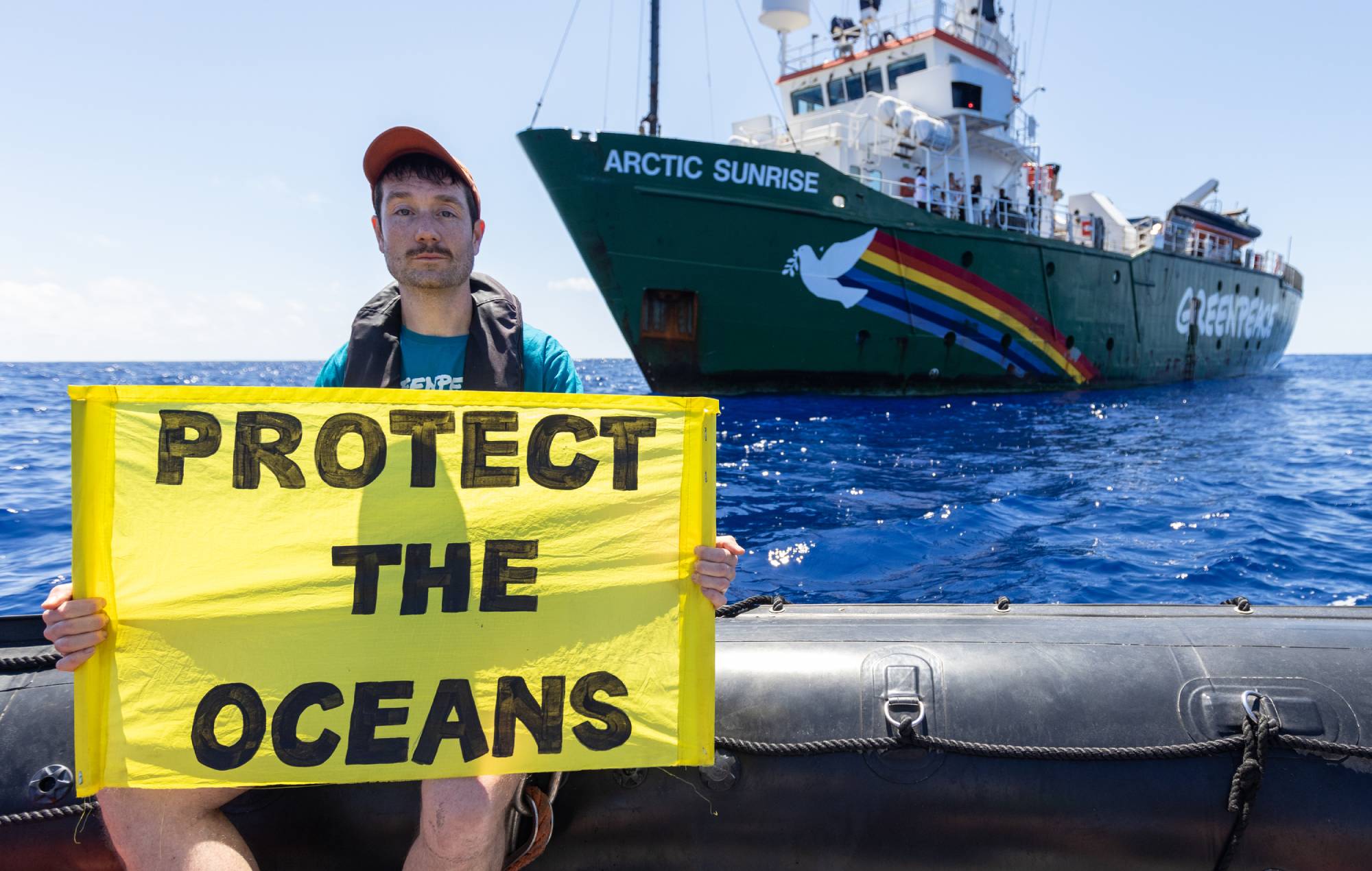 Dan Smith, Bastille sur un rhib devant l'Arctic Sunrise avec une bannière Protect the Oceans.  Crédit : Presse