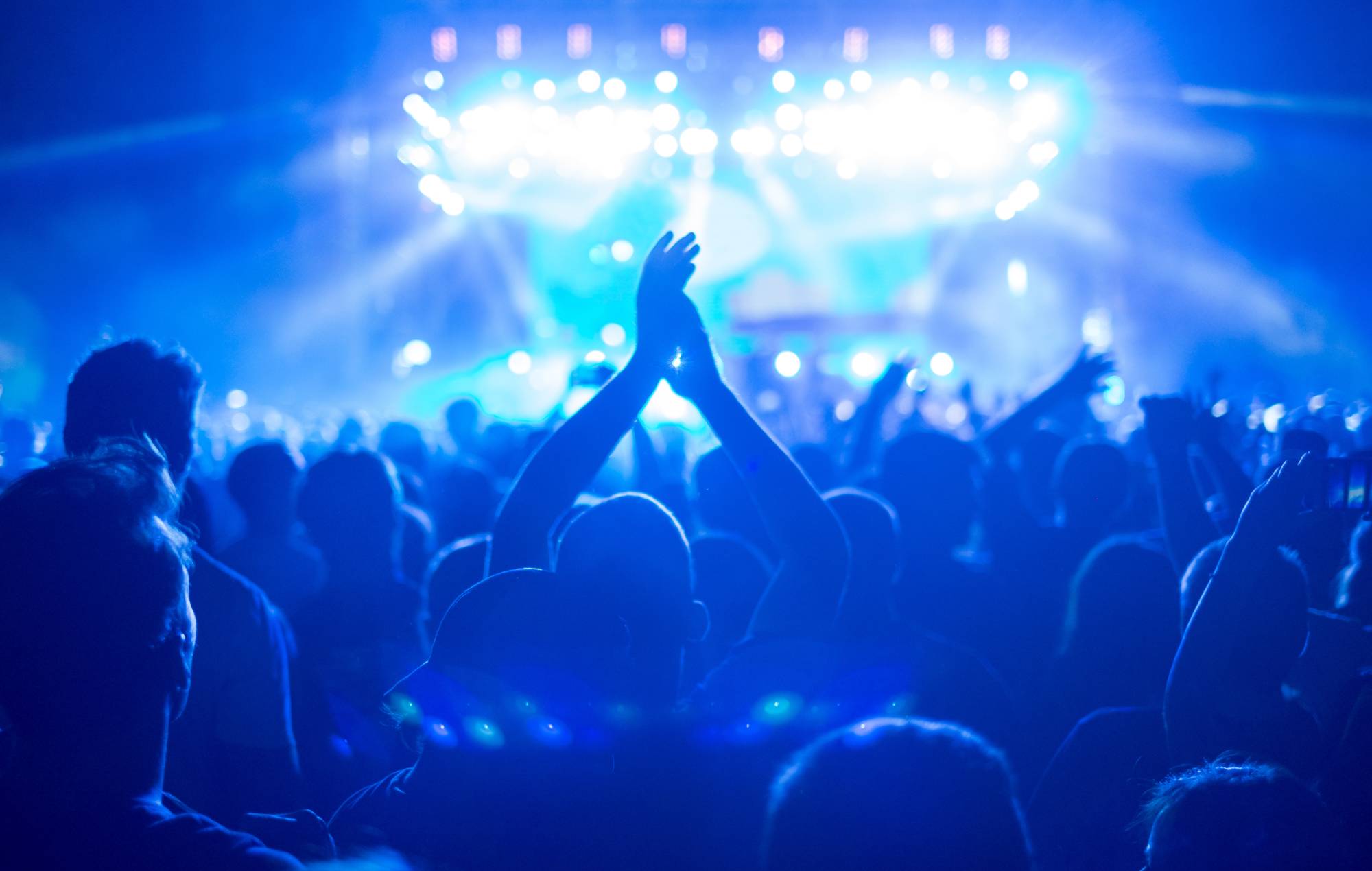 Photo d'une foule nombreuse lors d'un concert de musique, profitant d'un événement de festival de musique, avec des lumières bleues sur la scène et une mer de mains. Crédit : zoramn via GETTY