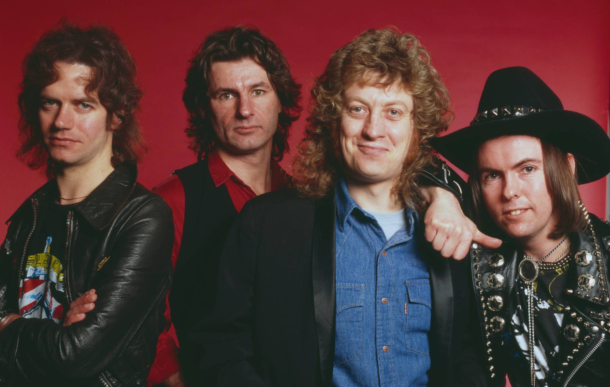 Portrait en studio du groupe de rock anglais Slade, posé à Londres vers 1975. Le groupe est, de gauche à droite : le bassiste Jim Lea, le batteur Don Powell, le chanteur Noddy Holder et le guitariste Dave Hill portant une veste en cuir avec des clous métalliques. (Photo de Michael Putland/Getty Images